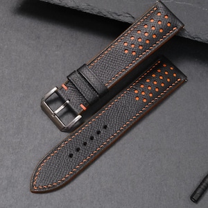 May include: Black watch strap with orange stitching and perforated holes. The strap has a stainless steel buckle and a matching black keeper. A small screwdriver is also included.