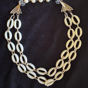 May include: Cream-colored vintage necklace with two strands of oval links and a delicate chain of small beads. The necklace features gold-toned metal accents and a secure clasp, perfect for adding a touch of retro elegance to any outfit.