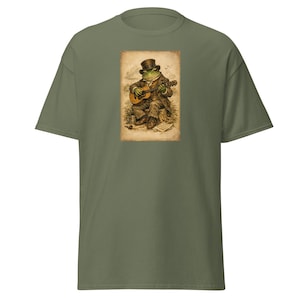 Könnte beinhalten: Olivgrünes T-Shirt mit einer Vintage-Illustration eines Frosches, der Gitarre spielt. Der Frosch ist in einem Anzug und Zylinder gekleidet, mit detailliertem Hintergrund. Die Grafik ist auf einem klassischen T-Shirt mit kurzen Ärmeln gedruckt.