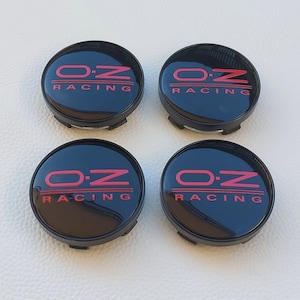 Puede incluir: Cuatro tapacubos negros con el texto rojo "OZ RACING". Las tapas son redondas con un acabado brillante. El texto está en negrita, con fuente sans-serif.