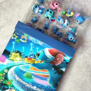 K&ouml;nnte beinhalten: Ein blauer Adventskalender mit der Figur Stitch, mit einer transparenten Kunststoffschale mit kleinen Stitch-Figuren. Der Kalender hat ein Winterthema mit Weihnachtsb&auml;umen und Zahlen. Die Figuren sind in verschiedenen Posen und Farben.