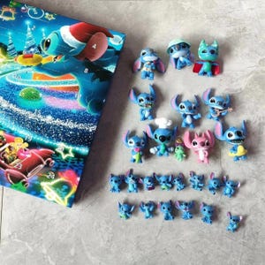 K&ouml;nnte beinhalten: Ein Adventskalender mit dem Charakter Stitch in Blau und Wei&szlig;. Der Kalender ist ge&ouml;ffnet und zeigt eine Reihe kleiner Stitch-Figuren in verschiedenen Posen und Outfits. Die Figuren sind blau, rosa und gr&uuml;n.