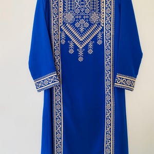 May include: A long, royal blue dress with long sleeves and intricate gold embroidery. The embroidery features floral and geometric patterns along the neckline, sleeves, and vertical panels. The dress is displayed on a white hanger.
