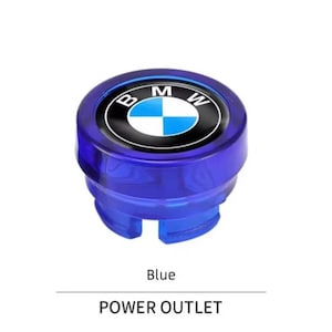 May include: A blue power outlet cover with the BMW logo at the centre. The logo is a black circle with the BMW letters and a blue and white chequered design. The word "Blue" is below the cover.