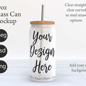 May include: A white 20 ounce glass can mockup with a wooden lid and a clear straw. The can has the text "Your Design Here" printed on it. The can is sitting on a white wooden surface.