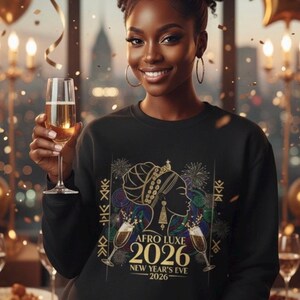 May include: A woman wearing a black sweatshirt with the text "AFRO LUXE 2026 NEW YEAR'S EVE 2026" and a graphic of a woman's silhouette. She is holding a champagne flute. The background includes gold balloons and confetti.