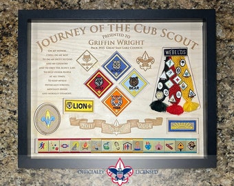 May include: A framed wooden plaque with a light brown background, displaying a Cub Scout's journey. The plaque features the Scout Oath, a collection of merit badges, and the words "Journey of the Cub Scout" and "Presented to Griffin Wright".