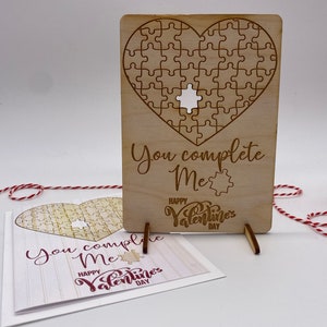 May include: A wooden Valentine's Day card with a heart-shaped puzzle. The puzzle has a missing piece. The card reads "You complete me" and "Happy Valentine's Day".
