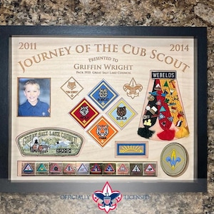 May include: Framed Cub Scout memorabilia display. Features a photo, badges, and text reading "2011 Journey of the Cub Scout 2014" and "Griffin Wright." Includes a black frame and the text "Officially Licensed."
