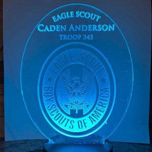 May include: A blue acrylic plaque with the text "Eagle Scout Caden Anderson Troop 345" and a Boy Scouts of America logo with an eagle and the text "Be Prepared".
