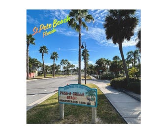 May include: A street scene in St. Pete Beach, Florida, with palm trees lining the road under a blue sky. A sign reads "Pass-A-Grille Beach, Homesteaded 1886."
