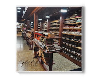 May include: Interior shot of a cigar shop with wooden shelves and display cases filled with cigars. The shop has a vintage feel with warm lighting and the text "Ybor City FLORIDA" in an elegant script.