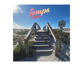 May include: A wooden boardwalk with stairs leads to a beach under a bright blue sky. The word "Tampa Florida" is written across the top in a gradient of pink and yellow. A sign on the right indicates beach access and parking.