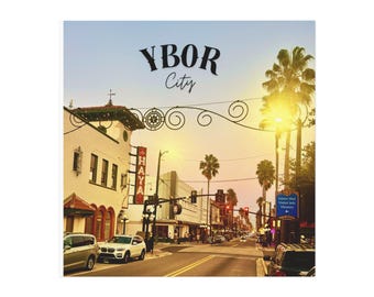 May include: A square print featuring a street scene in Ybor City, Florida, with the text "YBOR City" at the top. The image shows buildings, palm trees, cars, and streetlights under a sunset sky.