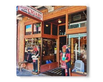 May include: Exterior shot of a cigar shop with a sign that reads "NICARAGUANA CIGARS HAND ROLLED CIGARS". Two wooden statues of Native Americans stand outside the entrance. The shop has large windows and a wooden door.