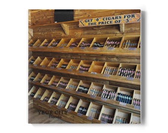 May include: Wooden display shelves filled with various cigars. The shelves are labeled "YBOR CITY Florida" and a sign reads "GET '6' CIGARS FOR THE PRICE OF '5'". The cigars are arranged in individual compartments, showcasing a variety of colors and styles.
