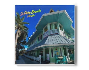 May include: A square tile featuring a building in St. Pete Beach, Florida, with a teal roof and green walls. The text "St. Pete Beach Florida" is in the upper left corner. Palm trees line the sidewalk in front of the building.
