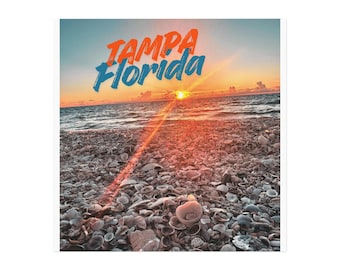 May include: A beach scene at sunset with the text "TAMPA Florida" in orange and blue. The foreground is covered in seashells, leading to the ocean under a vibrant sky. The sun is setting over the water.