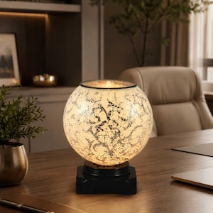 May include: A spherical lamp featuring a white and silver crackle glass finish with an intricate swirling pattern. The globe sits atop a solid black square base, emitting a warm, soft glow from within the textured glass surface.