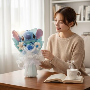 Puede incluir: Un ramo con un personaje alien&iacute;gena azul de peluche con grandes orejas, rodeado de flores de tela y envuelto en papel azul claro y blanco. El ramo se presenta en un jarr&oacute;n azul claro.