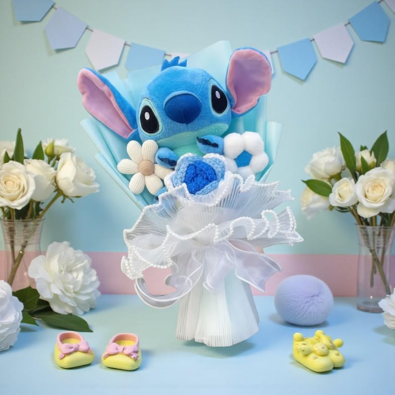 Puede incluir: Un ramo de peluche azul de Stitch con flores decorativas blancas y azules. El ramo est&aacute; envuelto en papel azul y tul blanco. Un par de zapatos de beb&eacute; amarillos con lazos rosas est&aacute;n en primer plano.