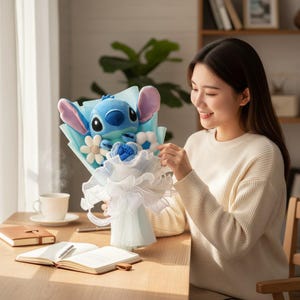 Puede incluir: Un ramo decorativo con un personaje de peluche Stitch azul, con grandes orejas, rodeado de elementos decorativos blancos y azules. El ramo est&aacute; envuelto en papel azul claro y tela blanca, creando un regalo caprichoso.