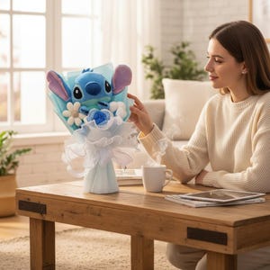 Puede incluir: Un ramo de peluche del personaje Stitch azul con detalles blancos y azules. El ramo est&aacute; envuelto en papel azul claro y cinta blanca. El ramo est&aacute; sobre una mesa de madera.