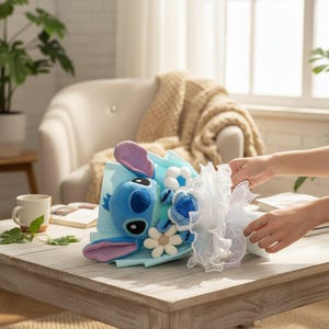 Puede incluir: Un ramo de personaje Stitch de peluche azul con detalles blancos y azules. El ramo incluye un peluche de Stitch, flores blancas y una cinta decorativa blanca. El ramo se presenta sobre un respaldo de papel azul claro.