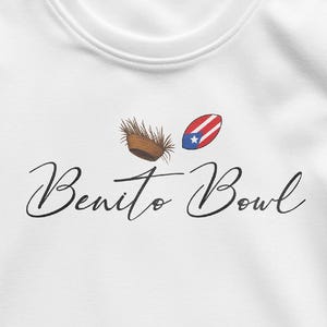 Op de afbeelding: Witte crewneck sweatshirt met de tekst "Benito Bowl" in cursief. Boven de tekst staan twee illustraties: een bruine, geweven kom en een rood, wit en blauw ontwerp met een ster.
