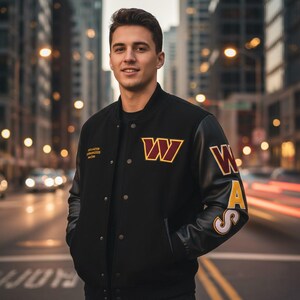 Może przedstawiać: Czarna kurtka typu varsity z rękawami ze skóry. Posiada logo drużyny "W" w kolorze bordowym i złotym na piersi i rękawie. Kurtka ma zapięcie na guziki i napis "Washington Commanders" na lewej piersi.