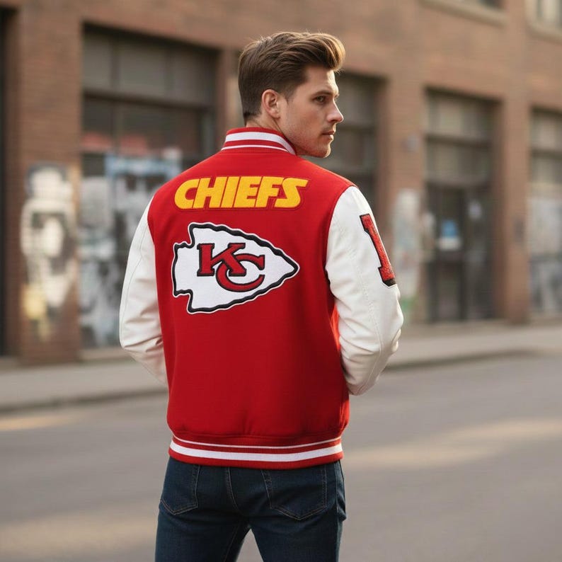 May include: Red and white varsity jacket with the word "CHIEFS" in yellow lettering across the back. The jacket features a team logo and white sleeves. The jacket is worn by a person in blue jeans.