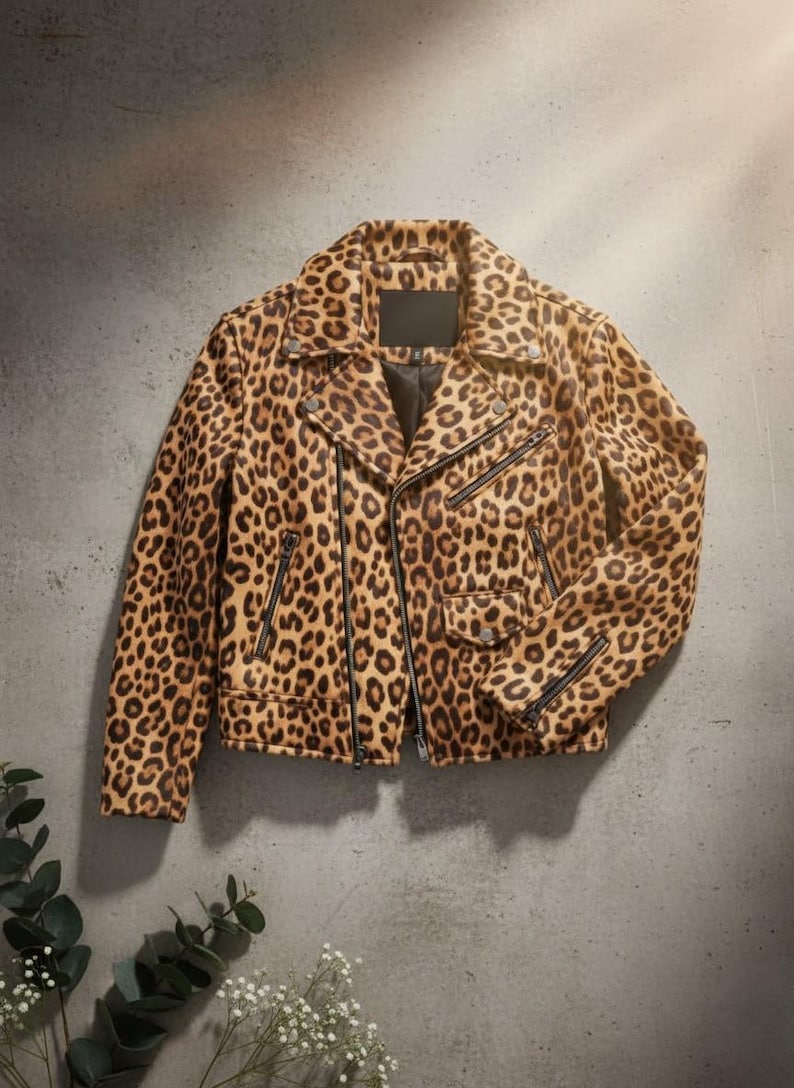 May include: A leopard print jacket with a classic biker style. The jacket features a notched collar, asymmetrical zip closure, multiple zip pockets, and a black lining. The animal print is a mix of brown and black spots on a tan background.