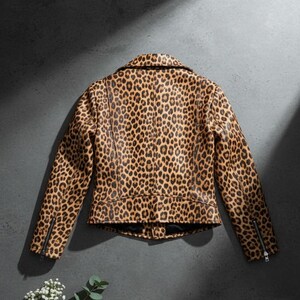 May include: A brown and black leopard print jacket with a classic collar and zipper details on the sleeves. The jacket is made of a faux leather material and has a fitted silhouette. The background is a dark gray.