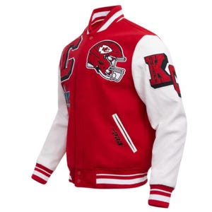 May include: Red and white varsity jacket with a football helmet patch and the letter "K". The jacket has white sleeves, a red body, and white stripes on the cuffs and hem. The jacket has a button-up front.