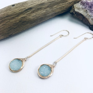 May include: A pair of long, silver earrings with a light blue, wire-wrapped, teardrop-shaped stone at the end of each earring.