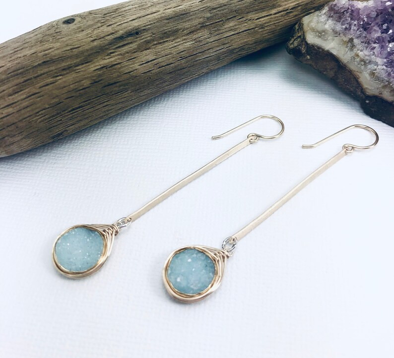 May include: A pair of long, silver earrings with a light blue, wire-wrapped, teardrop-shaped stone at the end of each earring.