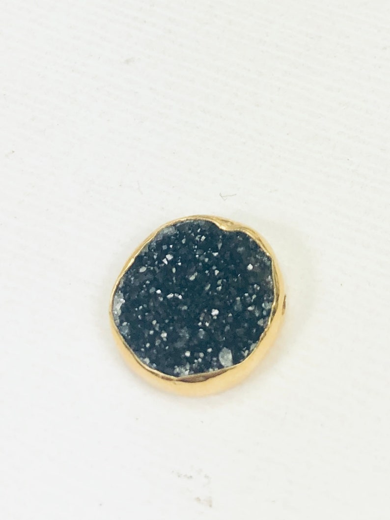 May include: A round, black, sparkly, gemstone pendant with a gold rim.