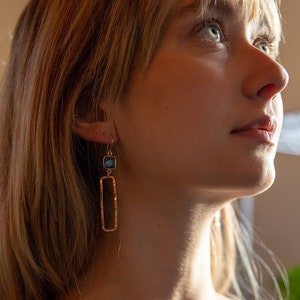 May include: A pair of gold earrings with a square blue gemstone and a long rectangular pendant.