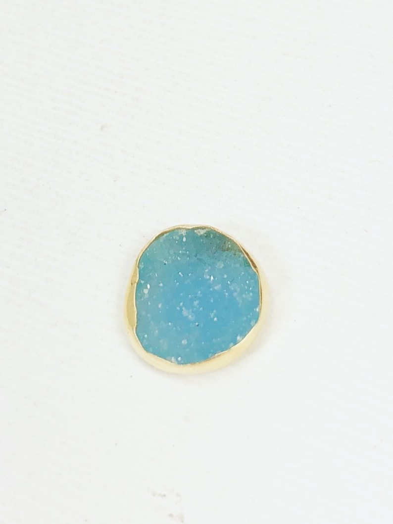 May include: A small, round, light blue stone with a gold rim. The stone has a speckled texture.