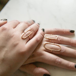 May include: Three gold rings with different sized oval shapes. The rings are on a person's fingers.