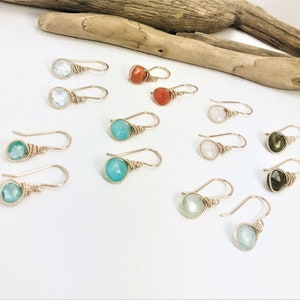 May include: Assortment of gemstone earrings with gold wire wrapping. The earrings feature various colors, including turquoise, green, white, and red.