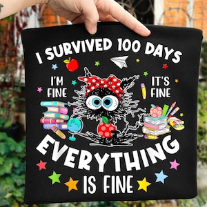 Könnte beinhalten: Schwarzes T-Shirt mit dem Text "I Survived 100 Days" und "Everything Is Fine". Das Design zeigt eine Cartoon-Katze mit großen Augen, einer roten Schleife mit Punkten und Illustrationen zum Thema Schule.
