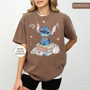 May include: Espresso-colored t-shirt featuring a cartoon Stitch character wearing glasses and a scarf, sitting atop a stack of books with an owl. The shirt has the text "MORE COLOR OPTIONS" on the left side.