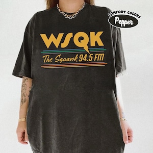 May include: Dark gray t-shirt with the text "WSQK The Squawk 94.5 FM" in yellow, green, blue, and orange. The shirt is a Comfort Colors Pepper brand.