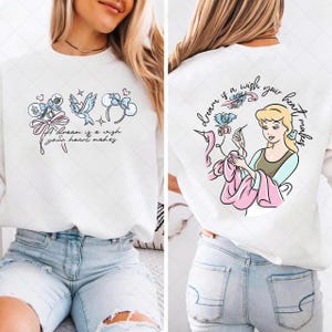 May include: White sweatshirt with a front graphic featuring a bow, bird, and headband design, with the text "A dream is a wish your heart makes." The back of the sweatshirt has a Cinderella graphic with the text "dream is a wish your heart makes."