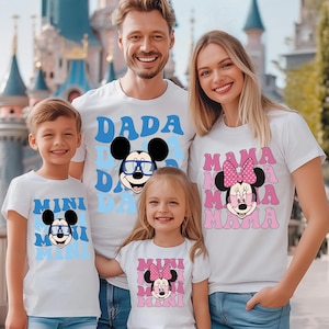 May include: A set of four white t-shirts featuring cartoon mouse graphics. Two shirts display blue text reading DADA and MINI with a mouse wearing blue glasses. Two shirts display pink text reading MAMA and MINI with a mouse wearing a pink bow.