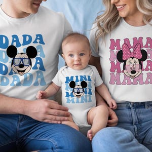 May include: A white t-shirt with blue DADA text and a Mickey Mouse graphic wearing blue glasses, a white baby bodysuit with blue MINI text and a Mickey Mouse graphic, and a white t-shirt with pink MAMA text and a Minnie Mouse graphic.