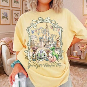 K&ouml;nnte beinhalten: Hellgelbes T-Shirt mit einem Disney-Motiv und dem Text "You've got a Friend in Me". Die Grafik zeigt Charaktere und ein Schloss. Das T-Shirt hat kurze &Auml;rmel und eine lockere Passform.