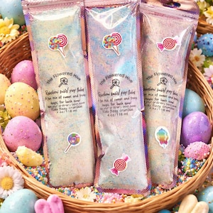 May include: Three clear pouches of bath fizzies with candy stickers, inside a woven basket with Easter eggs and flowers. The pouches read "Rainbow swirl pop tubes" and "Kids fizzy crumbles" with a net weight of 4 oz / 118 ml.