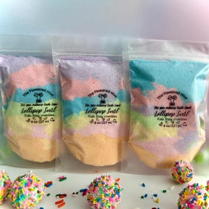 May include: Three clear plastic bags filled with colorful bath bomb crumbles. Each bag has a label that reads "The Flowered Hive Lollipop Swirl Kids fizzy crumbles 8 oz/227 ml." Sprinkled bath bombs are in front of the bags.